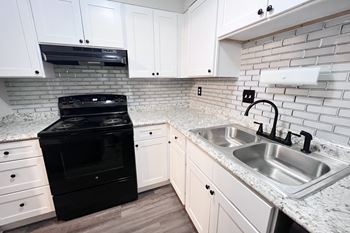 A black oven sits in a kitchen with white cabinets and a marble countertop.